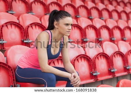 Side view of a serious toned young woman sitting on chair in the stadium