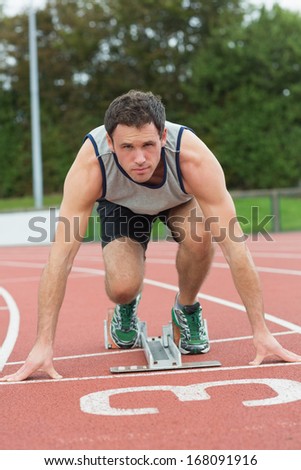 Full length portrait of a young man ready to race on running track