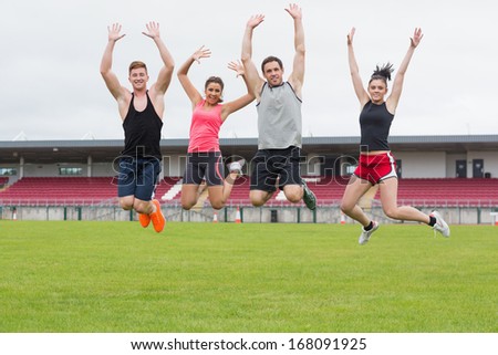 Full length portrait of young fit people jumping on ground against the stadium