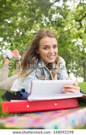 Cheerful student lying on the grass studying with her tablet pc on college campus
