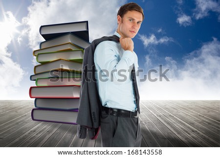 Serious businessman holding his jacket against stack of books against sky