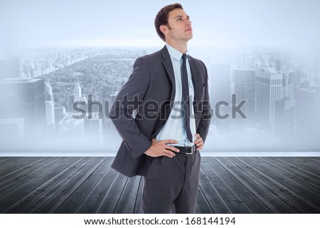 Serious businessman with hands on hips against city scene in a room
