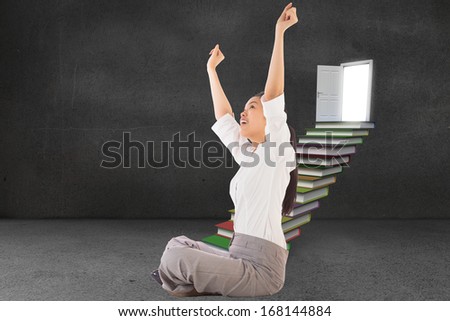 Businesswoman sitting cross legged cheering against steps made from books leading to door in grey room