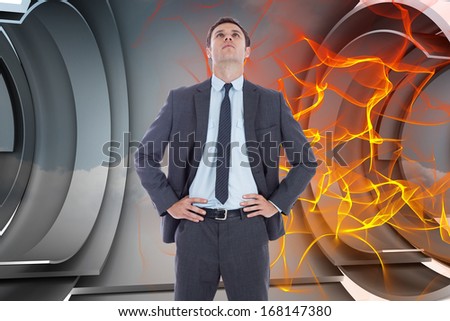Serious businessman with hands on hips against orange energy design on a futuristic structure