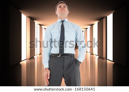 Serious businessman standing with hand in pocket against lit up black modern hallway