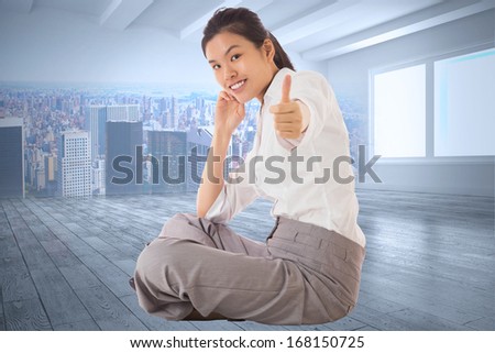 Businesswoman sitting cross legged showing thumb up against city scene in a room