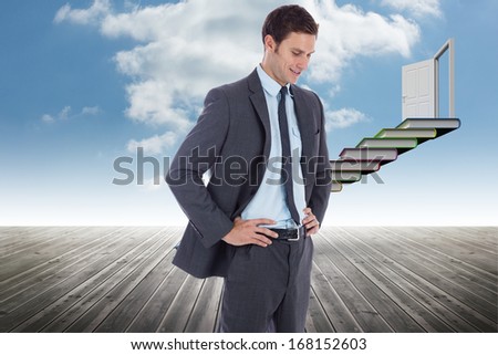 Smiling businessman with hands on hips against book steps leading to door against sky