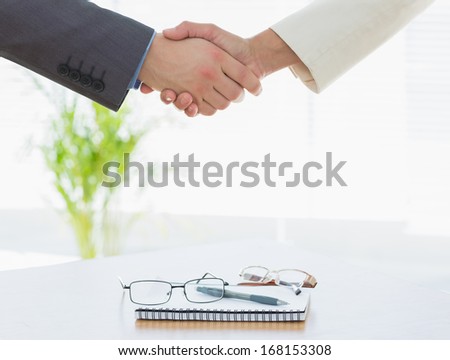 Close-up of shaking hands over eye glasses and diary after a business meeting at office desk