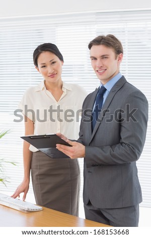 Portrait of two confident business colleagues standing with clipboard at office desk