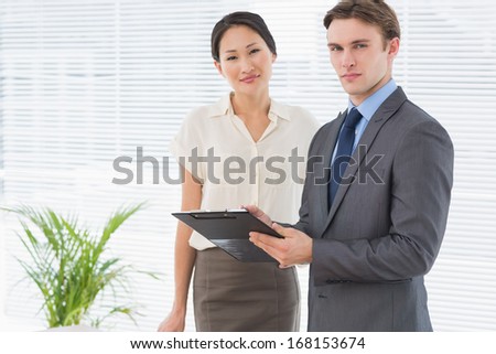 Portrait of two confident business colleagues standing with clipboard at office