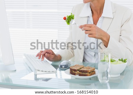 Mid section of a young businesswoman using computer while eating salad at office desk