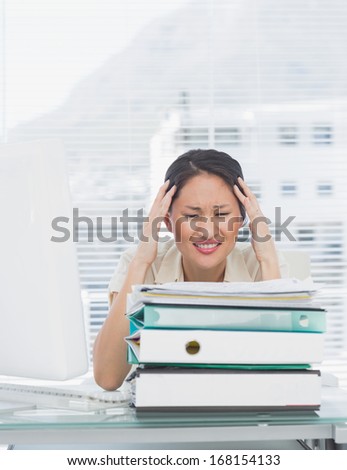Angry young businesswoman sitting with stack of folders at office desk
