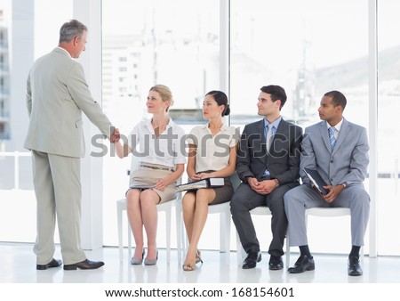 Businessman shaking hands with woman besides people waiting for job interview in a bright office