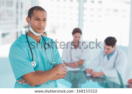 Serious male surgeon standing with group around table in background at hospital