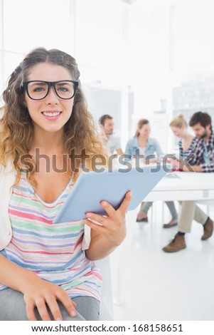 Smiling young woman using digital tablet with colleagues in background at a creative bright office