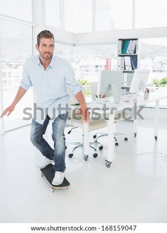 Full length of a happy young man skateboarding in a bright creative office