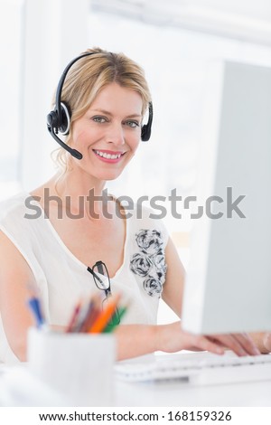 Portrait of a casual young woman with headset using computer in a bright office