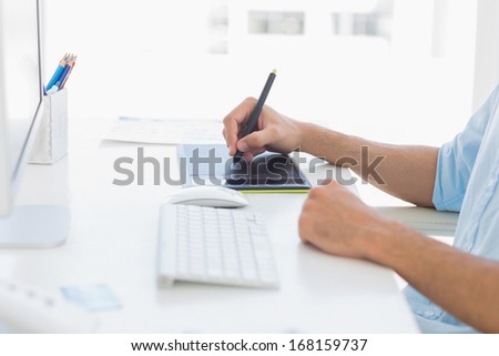 Close-up mid section of a casual male photo editor using graphics tablet in a bright office
