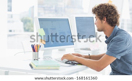 Side view of a concentrated casual young man using computer in a bright office