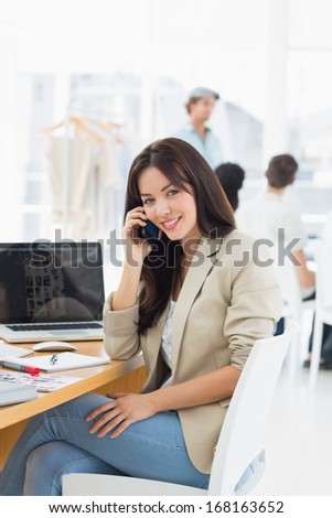 Casual young woman on call at desk with group of colleagues behind in a bright office