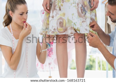 Two fashion designers adjusting dress on model in the studio