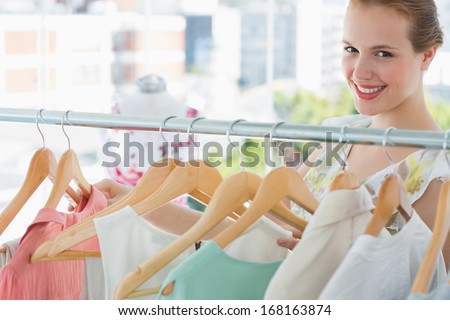 Close-up portrait of happy female customer selecting clothes at clothing rack in store