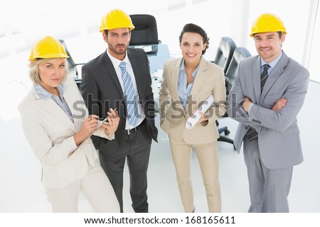 Portrait of well dressed confident architects with hard hats and blueprint standing in the office