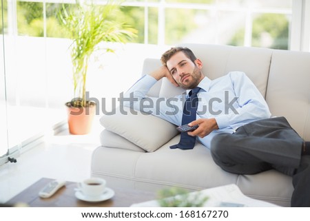 Relaxed well dressed young man watching tv in the living room at home