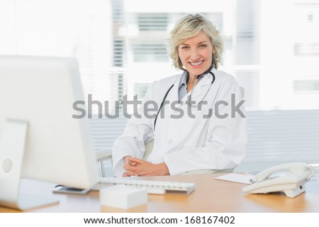 Portrait of a confident smiling female doctor sitting with computer at medical office
