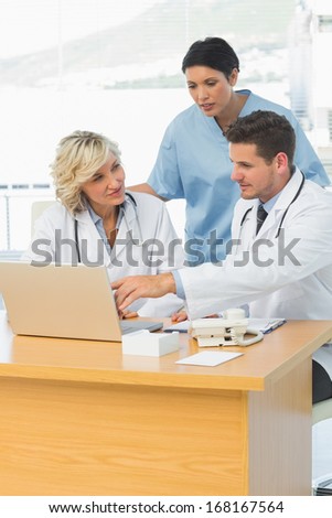 Three concentrated doctors using laptop together at the medical office