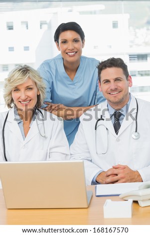 Portrait of three smiling doctors with laptop at the medical office