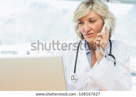 Concentrated female doctor using laptop and phone in the medical office