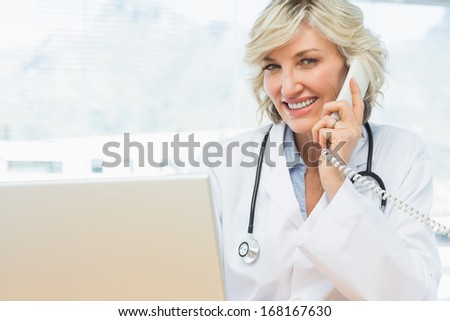 Portrait of a smiling female doctor using laptop and phone in the medical office
