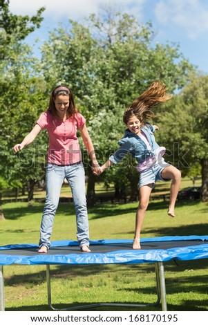 Full length of a happy girl and mother jumping high on trampoline in the park