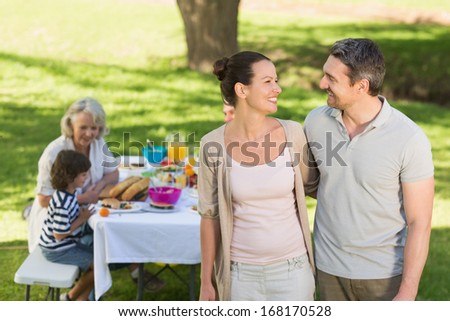 Couple with extended family dining background at outdoor table