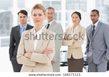Businesswoman looking at camera with team behind her in the office