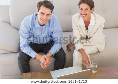Happy business partners looking at camera sitting on sofa in the office