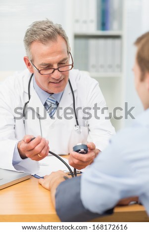 Smiling doctor taking his patients blood pressure in his office at the hospital