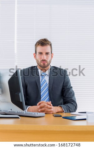 Portrait of a serious young businessman with computer at office desk