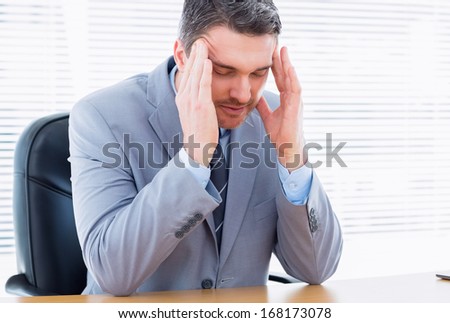 Young elegant businessman with severe headache sitting at office desk