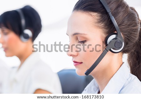 Close-up side view of a beautiful young female executive with headset in a bright office