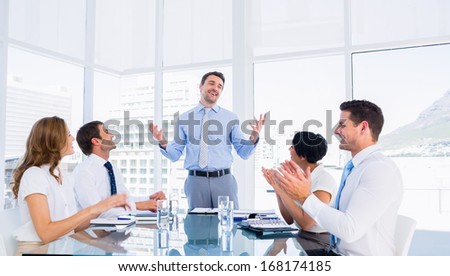 Business executives clapping around conference table in a bright office