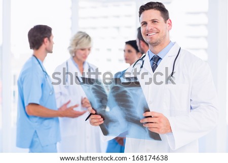 Smiling male doctor examining x-ray with colleagues standing behind in a medical office