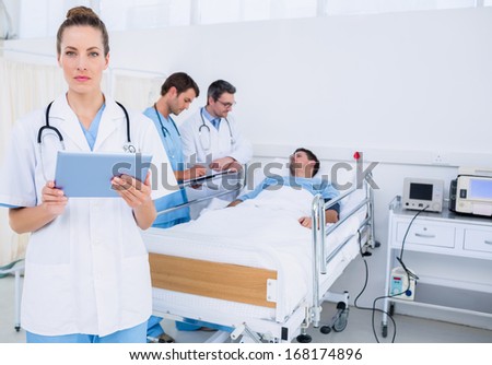 Female doctor using digital tablet with colleagues and patient behind in the hospital