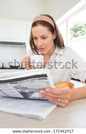 Young woman with coffee cup reading newspaper in the kitchen at home