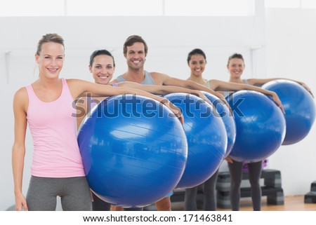 Portrait of an instructor and fitness class holding exercise balls at fitness studio