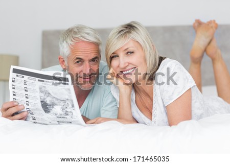 Portrait of a smiling mature couple reading newspaper in bed at home