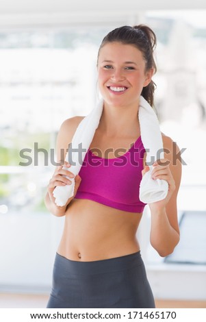 Portrait of a smiling fit young woman with towel standing in the gym