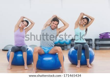 Portrait of smiling young people sitting on exercise balls and stretching hands in the gym