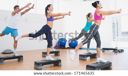 Female instructor with fitness class performing step aerobics exercise in gym